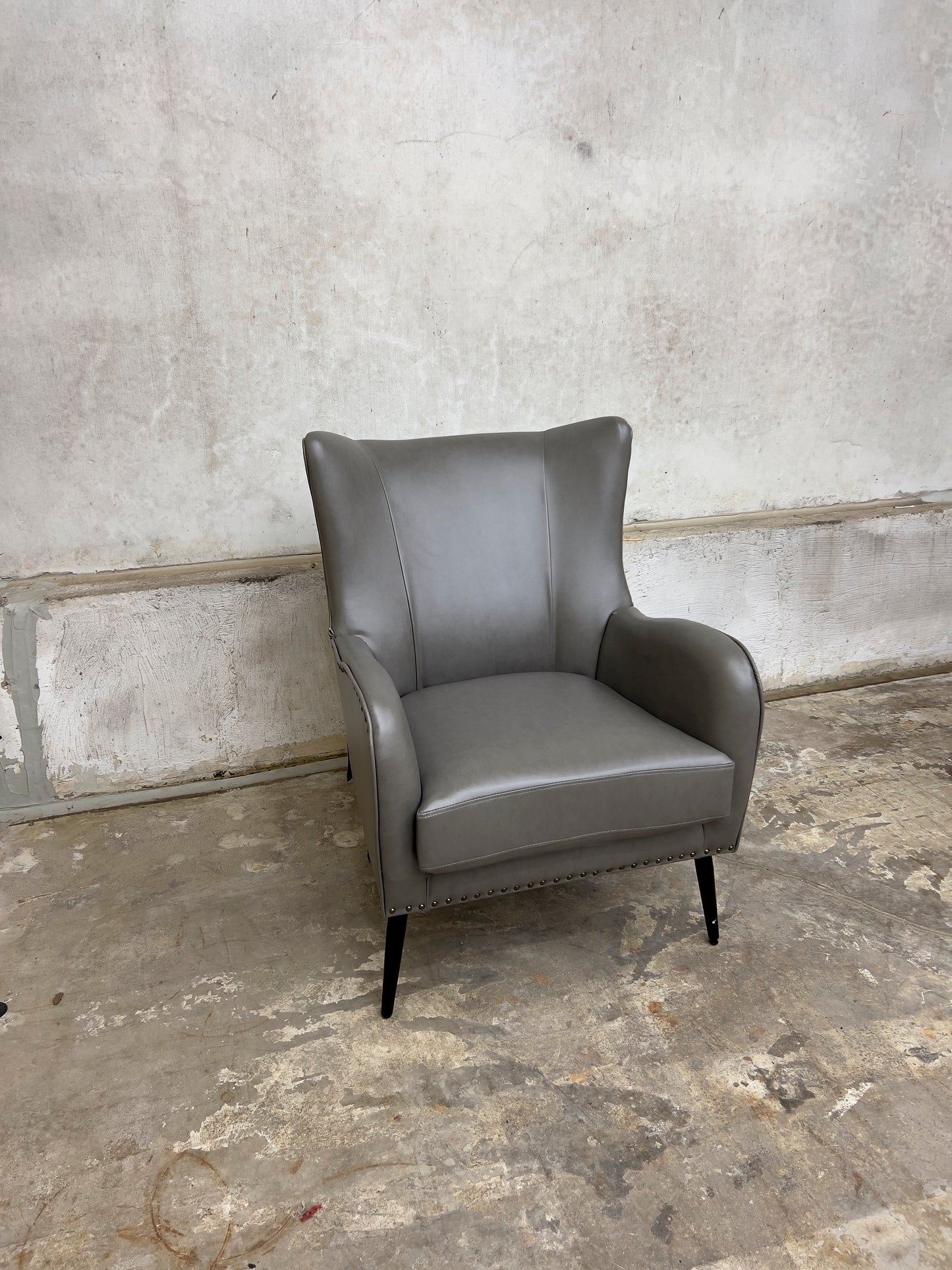 Grey Armchair, which features vegan leather upholstery, nailhead trim, and metal legs.